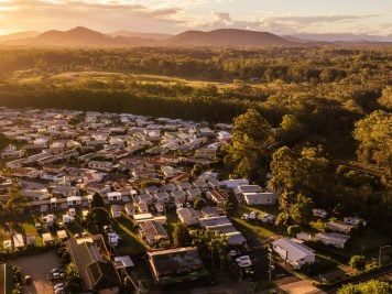 Aerial view of a Lifestyle Estate in Nambucca Heads, nestled among dense trees and hills under a golden sunset sky, with mountains visible in the distance.