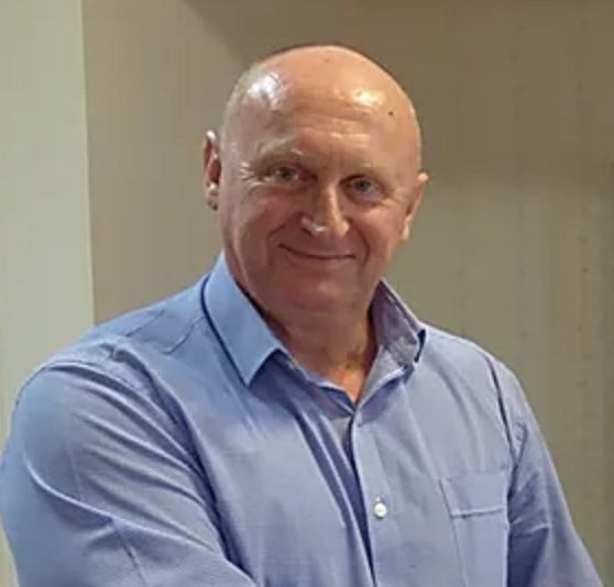 Steve Bowmaker, a middle-aged man with a bald head, is smiling. He is wearing a light blue buttoned-down shirt and standing indoors against a neutral background.