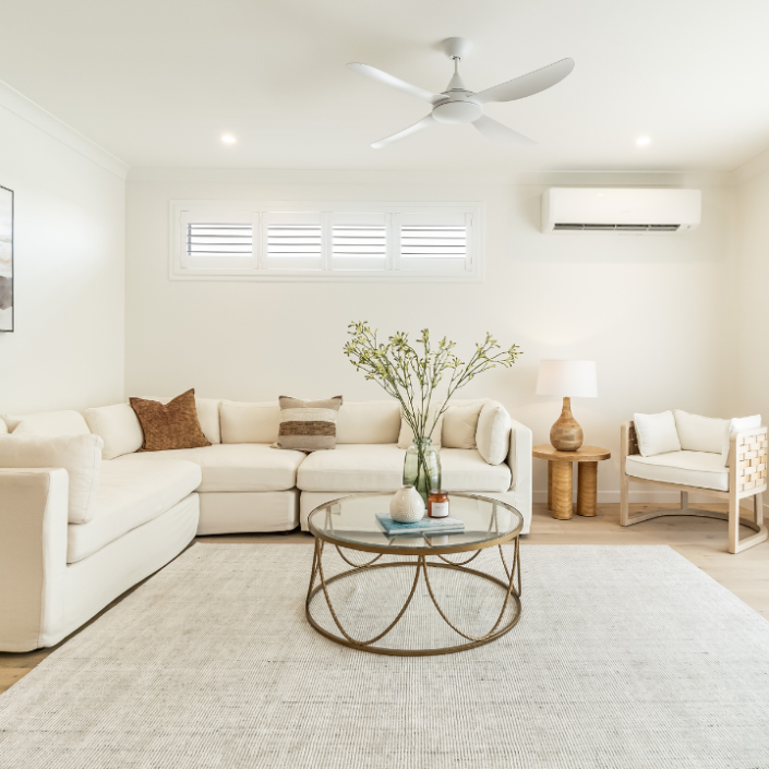 Bright, modern living room in Bancroft’s Lot 220, featuring a large white sectional sofa, round glass coffee table, light area rug, potted plant, wooden chair, wall art and sheer curtains—perfect for showcasing prime property.